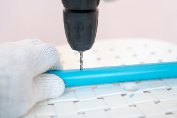 Close-up hand of man wearing cloth gloves and using a cordless drill to bore a hole a plastic (PVC) pipe.