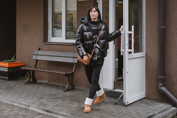 Urban lifestyle shot of woman with handbag opening white door, returning home or visiting business in city neighborhood. Woman going for walk