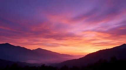 Fototapeta premium A majestic sunrise paints the sky with vibrant purples pinks and oranges over silhouetted mountain ranges and a misty valley