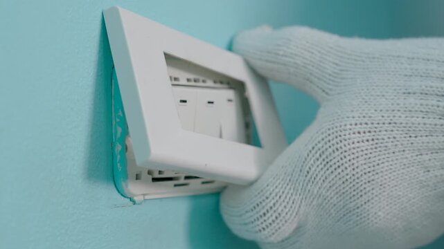 Close-up hand of man wearing cloth gloves and opening light switch cover to install or repair.
