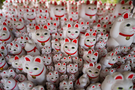 Dense grouping of white lucky cat statues with red details and gold bells, all facing forward in a vibrant display at Gotokuji Temple in Tokyo. The image highlights repetition, playful expressions