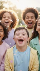 Obraz premium Happy boy with Down syndrome laughing with diverse group of friends. Vertical photo of inclusive childhood celebration with falling confetti outdoors. Joyful multiethnic kids representing friendship