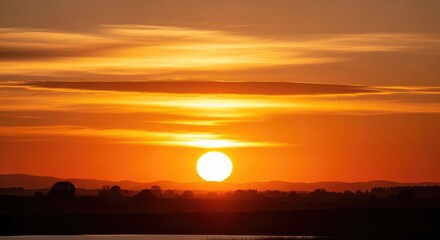 Golden sunset over a tranquil lake with a silhouette of a mountain range in the distance.