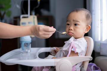 Mother feeding sick child in high chair at hospital