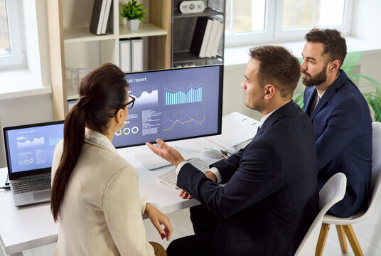 Business analysts meeting finance analytics dashboard report. Team reviews charts on monitor and laptop, discussing data driven decisions. Concept finance analytics teamwork strategy.