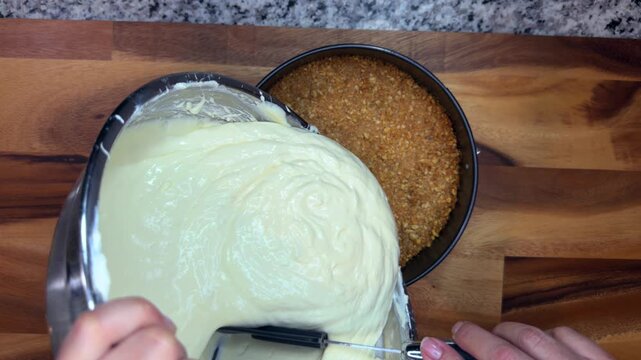 overhead shot of person pouring creamy cheesecake filling into a springform pan with graham cracker crust