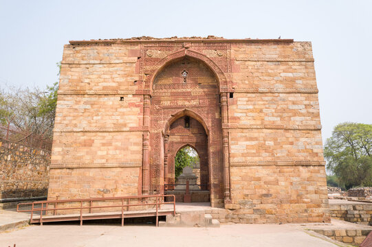 Wide view of the ornate stone gateway at the Tomb of Iltutmish in the Qutub Minar complex, Delhi. Detailed red sandstone arches and weathered masonry are highlighted by soft daylight, with greenery