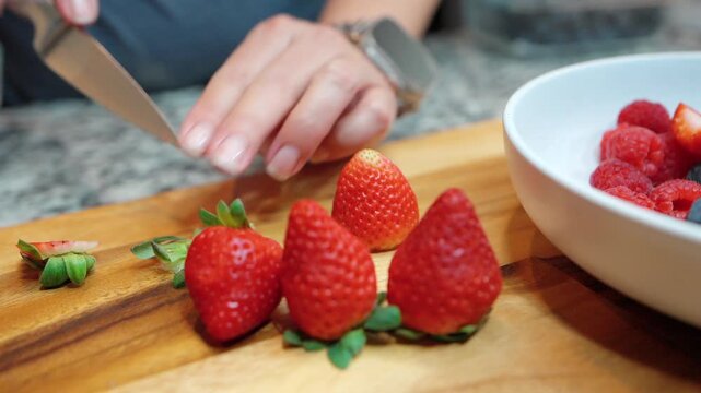 close up of person slicing fresh strawberries on a wooden board for a mixed fruit bowl