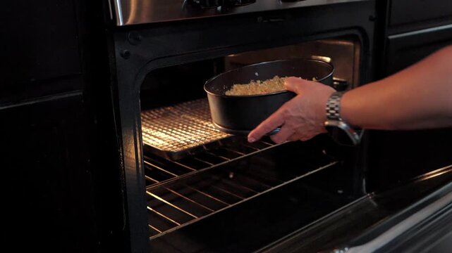 person placing a springform pan with cheesecake crust into a modern stainless steel oven