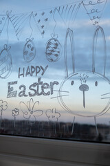 HAPPY EASTER text on creative painted window with white marker. Easter bunny rabbit decoration on big clear window. Springtime idea home decoration. Holiday preparation 