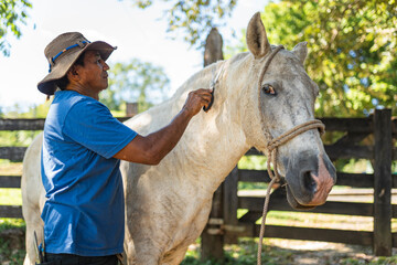 Smiling Costa Rican cowboy working with horse in rustic stable