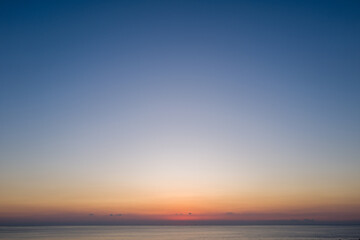 Obraz premium Expansive view of the calm sea beneath a wide open sky, fading from deep blue to warm orange hues at sunset in Kushimoto, Japan.
