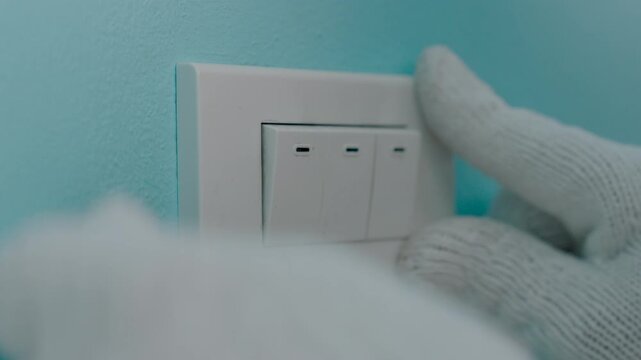Close-up hand of man wearing cloth gloves and closing light switch cover to install or repair.