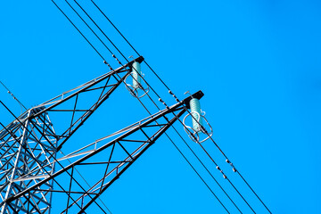 High voltage power lines carry electricity under a clear blue sky in broad daylight