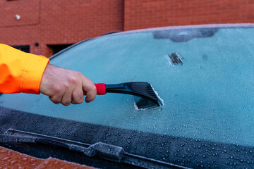 Person scrapes ice from car windshield in cold weather during morning hours in a city area