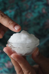 Hand holding a small glass bowl filled coconut oil 