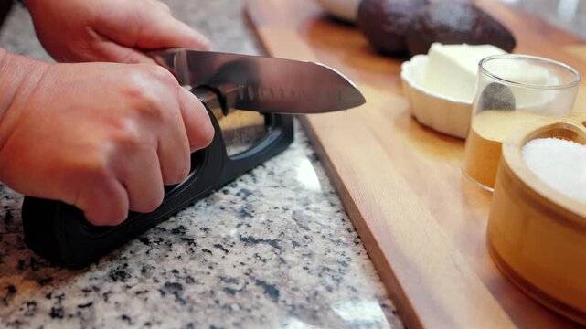close-up of person sharpening a steel chef knife with a manual pull-through sharpener in a kitchen