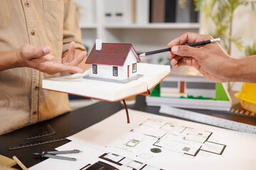 
Two people are working on a house plan design. They are using various tools, working with the...