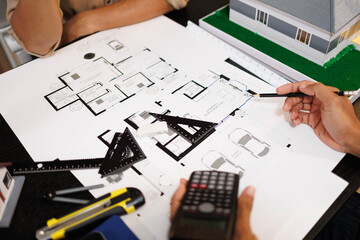 
Two people are working on a house plan design. They are using various tools, working with the...