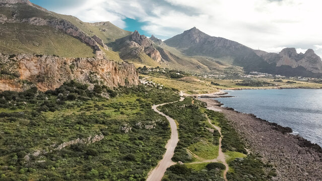 Aerial View Of San Vito Lo Capo In Sicily: Coastal Road Winding Through Green Mediterranean Landscape Toward Southern Rock Climbing Cliffs And Limestone Mountains