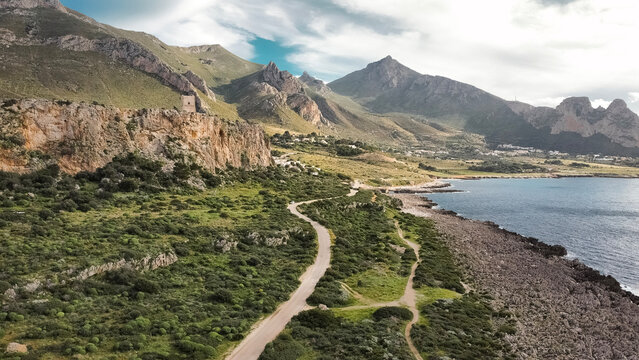 Aerial View Of San Vito Lo Capo In Sicily: Coastal Road Winding Through Green Mediterranean Landscape Toward Southern Rock Climbing Cliffs And Limestone Mountains