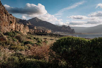 Naklejka premium Limestone Rock Climbing Cliff In San Vito Lo Capo, Sicily: Steep Orange And White Coastal Crag Rising Above Mediterranean Vegetation Under Clear Sky