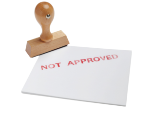 A wooden stamp beside a white card, prominently displaying the red text "NOT APPROVED.