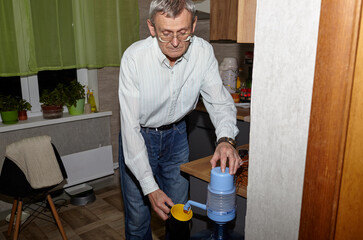 A man pours drinking water into a cup using hand pump. Drinking water is poured from water cooler bottle