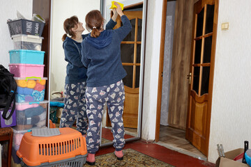 Woman with eyeglasses wiping mirror with napkin while doing house cleaning chores at home. Daily home chores, wet cleaning