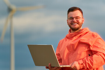 Engineer checking data with computer near windmill