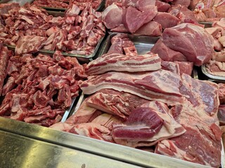 A high-angle, wide-view of various cuts of raw pork displayed in a commercial market setting.