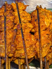 A high-angle view of traditional grilled boneless chicken (Kai Yang) displayed at an outdoor market.