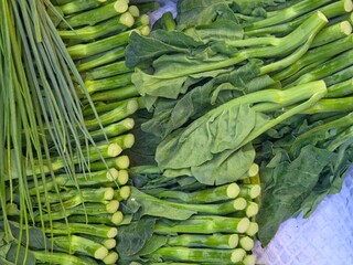 Top-down view of fresh leafy green vegetables, specifically Chinese broccoli (Gai Lan) and green onions, displayed at a market.