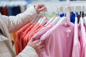 Shopper picks up clothing items from rack in store while browsing for new outfits during daytime