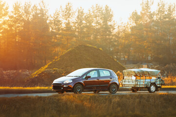 Naklejka premium Compact car with utility trailer driving on empty road
