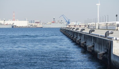 Wide perspective of a concrete harbor pier with large ships in the distance