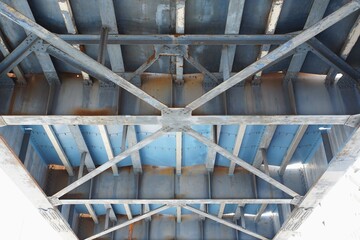 Detailed perspective of the weathered underside of a blue steel bridge