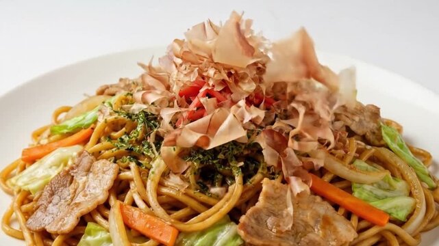 A captivating close-up captures a delicious and colorful savory dish being dynamically garnished with light, delicate flakes and bright red pickled elements, falling gracefully onto the plate. This ap