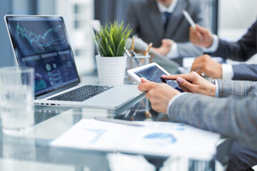 business documents on office table with smart phone and laptop computer and graph business with social network diagram and three colleagues discussing data in the background