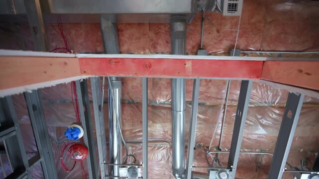  POV of an HVAC system under installation with exposed airducts, insulation, and metal framing inside a building. Ventilation, climate control construction work.
