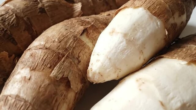 A close-up captures several raw cassava roots, some displaying their textured brown skin while others are partially peeled, revealing the vibrant white, starchy interior. This detailed shot emphasizes