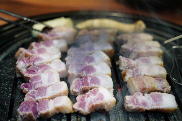 Sizzling Korean pork belly (samgyeopsal) grilling on a hot barbecue grill plate