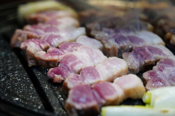 Sizzling Korean pork belly (samgyeopsal) grilling on a hot barbecue grill plate