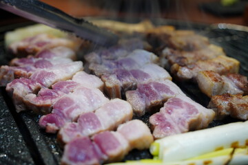 Sizzling Korean pork belly (samgyeopsal) grilling on a hot barbecue grill plate