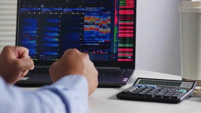 Over-the-shoulder view of a crypto trader analyzing crypto and stock charts live on a laptop, with a happy and excited expression. Concepts of Business, Stocks, and Crypto Trading.