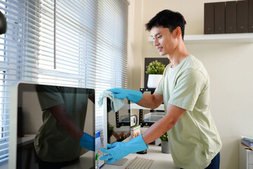 Worker in blue gloves using detergent to wipe computer screen during wet cleaning in office