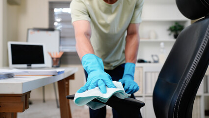 asian man cleaning and organizing an office desk with a computer and chair promoting tidiness and productivity