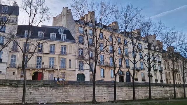 View from a cruising boat along the Seine river to the classic Parisian apartment buildings. Elegant Haussmann style facades and rows of trees with autumn leaves line the stone embankment