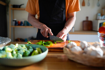 Hands, man and cutting with vegetables for health, nutrition or vegan diet for wellness. Male person, groceries and wood board in kitchen for cooking with food and ingredients to prepare home dinner