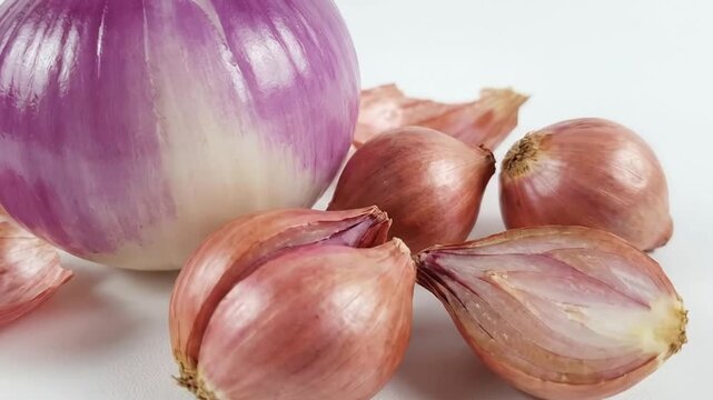 A vibrant close-up shot showcases a selection of fresh, organic onions and shallots arranged on a clean white background. A large, beautifully peeled purple onion stands prominently, revealing its dis